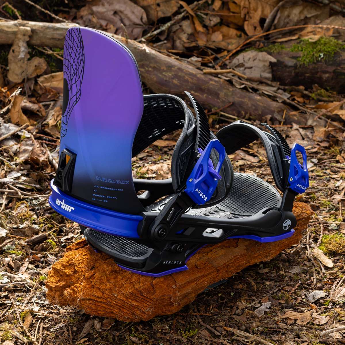 Arbor Hemlock Snowboard Bindings 2024 - Black bindings with purple accents and a black strap on top of a wood log in the woods.