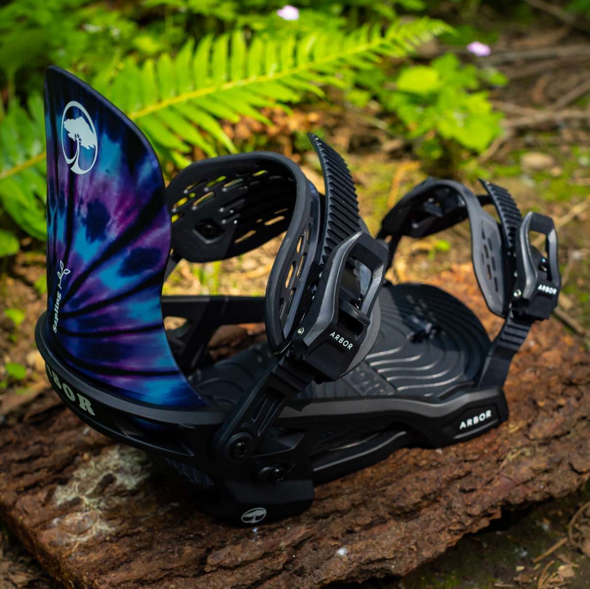 Arbor Sapling Youth Snowboard Bindings 2024 - A pair of black snowboard bindings with a white logo on top, featuring a tie-dye pattern on the straps.