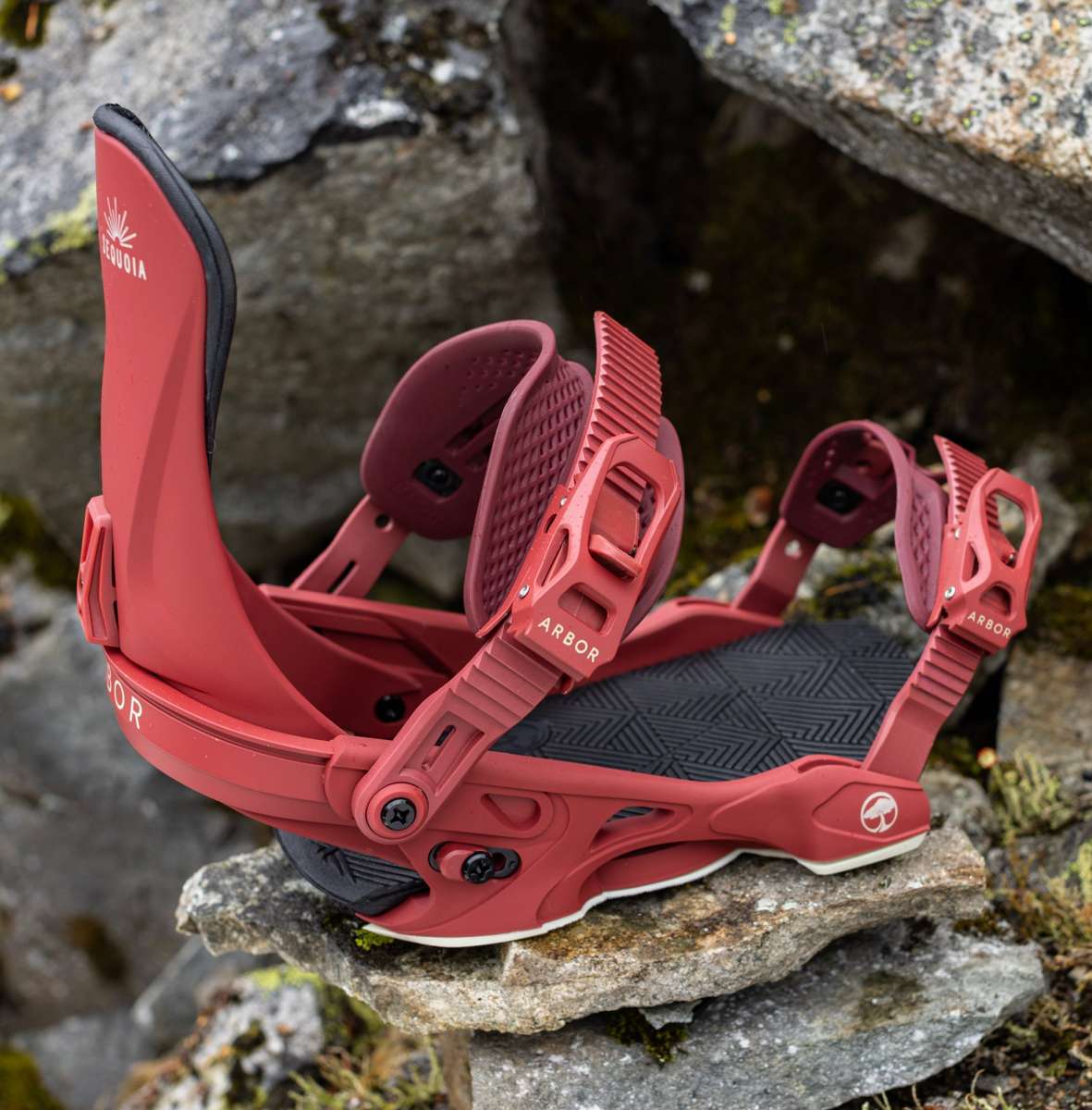 Arbor Women's Sequoia Snowboard Bindings 2024 - A pair of red snowboard bindings with white lettering and a black base plate, sitting on rocks.