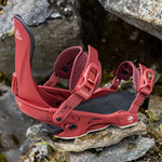 Arbor Women's Sequoia Snowboard Bindings 2024 - A pair of red snowboard bindings with white lettering and a black base plate, sitting on rocks.