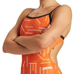 Arena Women's Puzzled Challenge Back One Piece Swimsuit - A woman with brown hair in a bun wears an orange one-piece swimsuit with white geometric lines and black trim around the edges.