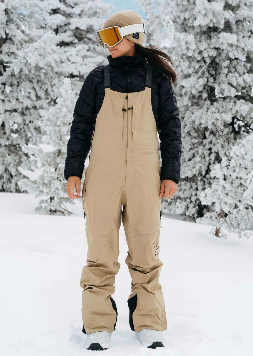 Burton Women's AK Gore-Tex Kimmy Bib Pant 2023 - A pair of tan snow pants with black accents and a zippered pocket on the thigh.