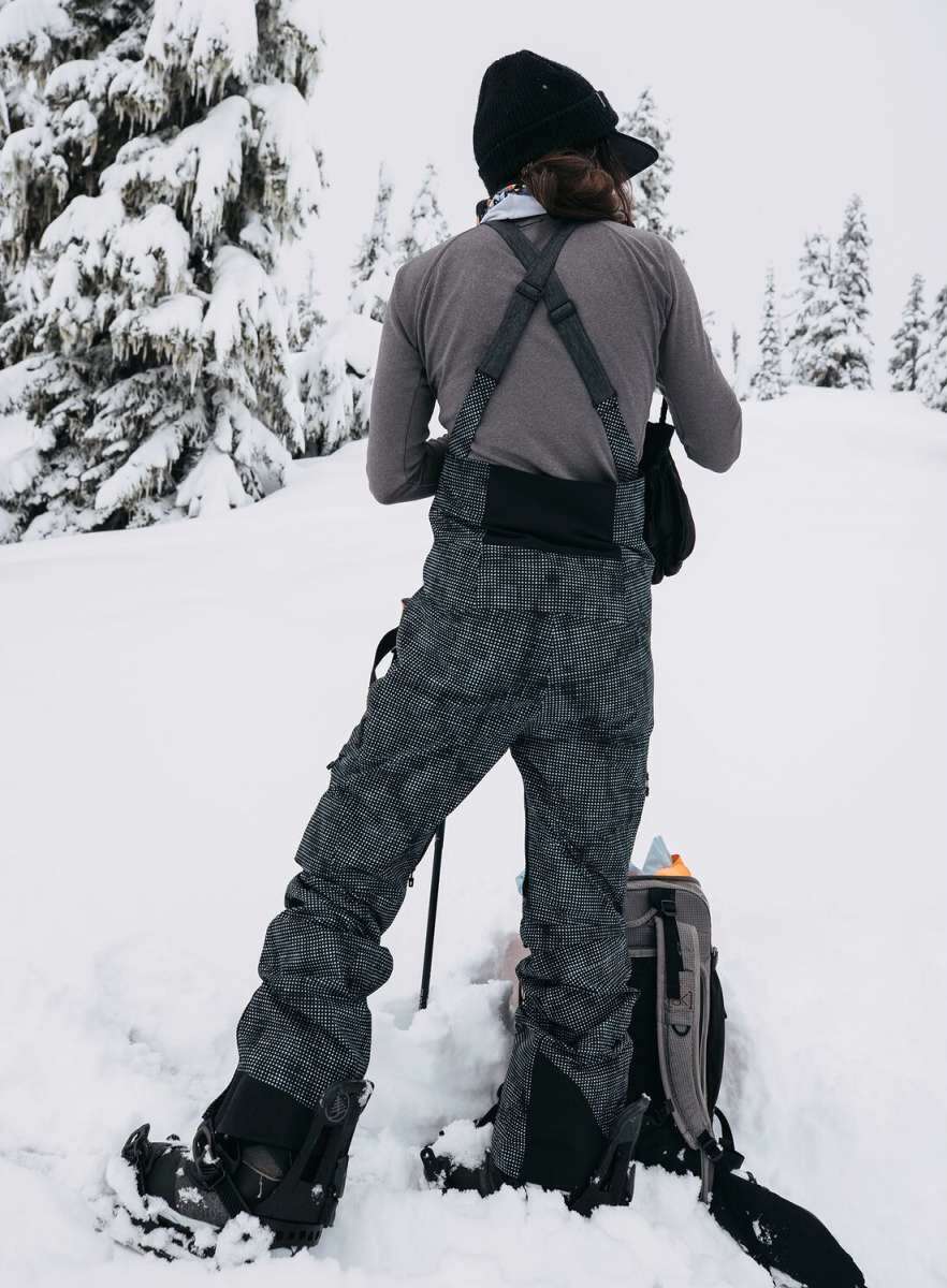 Burton Women's AK Gore-Tex Kimmy Bib Pant 2023 - Black bib pants with white stitching and a zippered pocket on the right thigh.