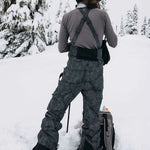 Burton Women's AK Gore-Tex Kimmy Bib Pant 2023 - Black bib pants with white stitching and a zippered pocket on the right thigh.