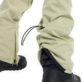 Burton Women's Gloria 2 Layer Stretch Pant 2024 - A pair of khaki-colored snow pants with a zippered pocket on the left thigh and a black drawstring at the waist.