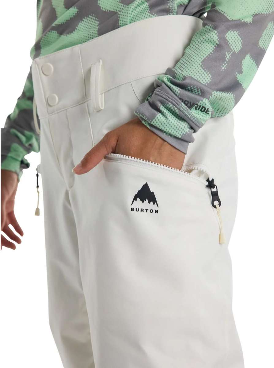 Burton Women's Marcy High Rise Stretch Pants 2024 - A pair of white snow pants with a black logo on the left thigh and a zipper pocket on the right side.