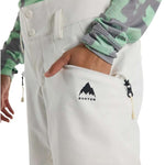 Burton Women's Marcy High Rise Stretch Pants 2024 - A pair of white snow pants with a black logo on the left thigh and a zipper pocket on the right side.