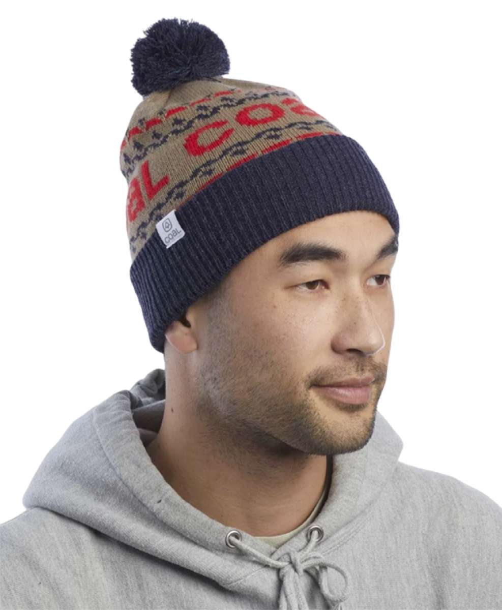 Coal Kelso Tall Pom Beanie 2023 - A tan beanie with a red and black patterned band around the crown, featuring a dark blue pom-pom on top.