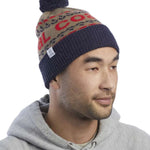 Coal Kelso Tall Pom Beanie 2023 - A tan beanie with a red and black patterned band around the crown, featuring a dark blue pom-pom on top.