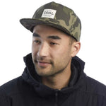 Coal Uniform Cap 2023 - A camouflage cap with a white rectangular patch on the front featuring the word "COAL" in black letters.