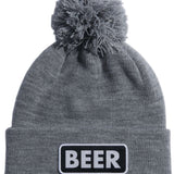 Coal Vice Mid Length Pom Beanie 2023 - A gray beanie with a large, fluffy pom-pom on top and a black patch that says "BEER" in white letters.