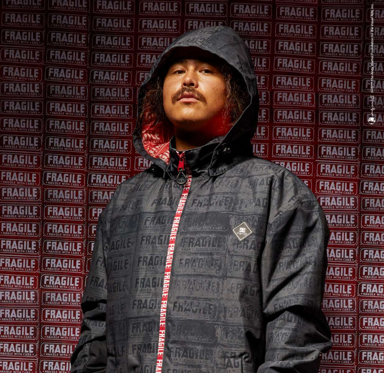 DC AW Vista Shell Jacket 2024 - A black jacket with a subtle pattern of white lines and logos, featuring a red zipper and a hood.