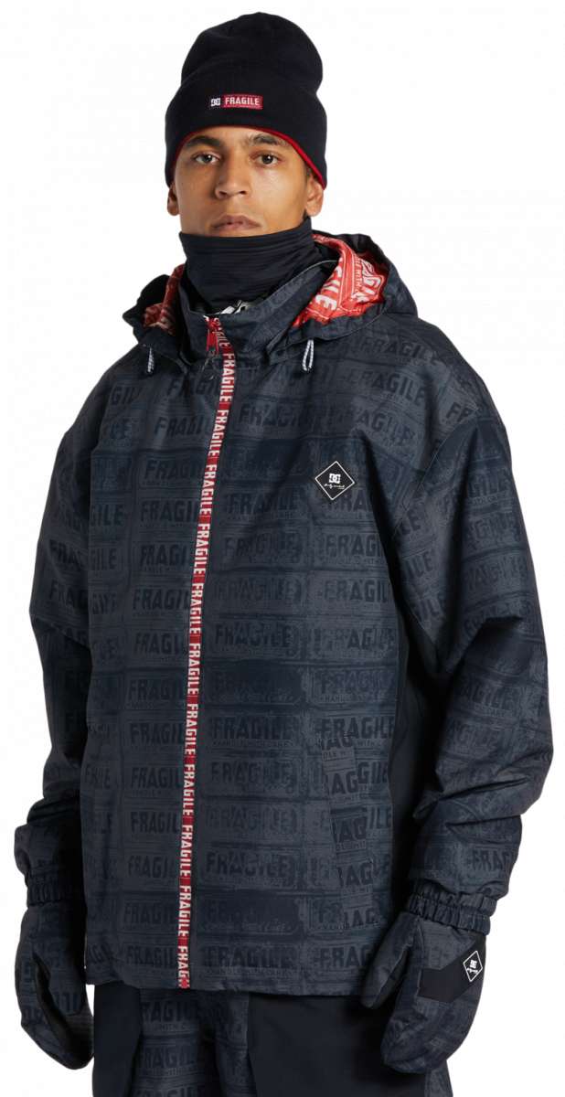 DC AW Vista Shell Jacket 2024 - A black jacket with a repeating pattern of "FRAGILE" labels in gray, featuring red accents on the hood and zipper.