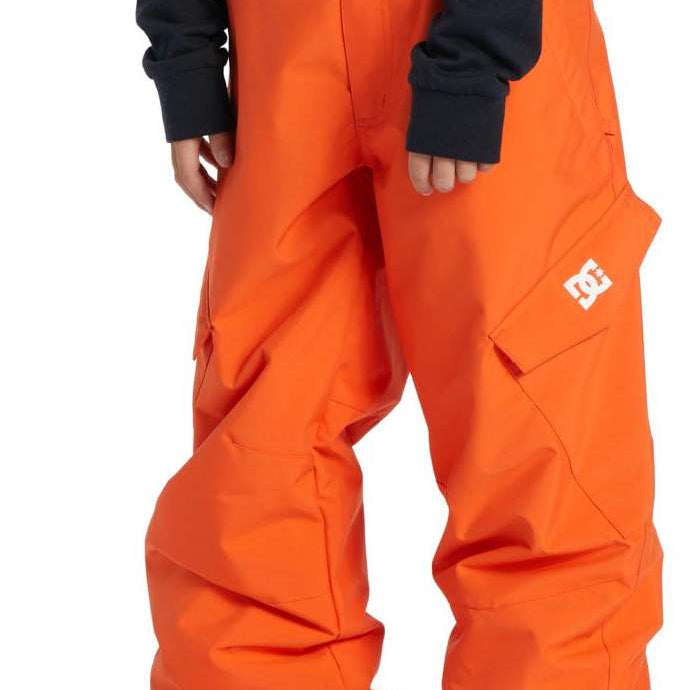 DC Youth Banshee Insulated Pant 2024 - A pair of bright orange snow pants with a white DC logo on the left leg, featuring two front pockets and adjustable Velcro straps at the waist.