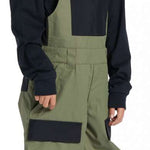 DC Youth Roadblock Insulated Bib 2024 - A pair of olive green and black insulated bib overalls with a white DC logo on the chest pocket.