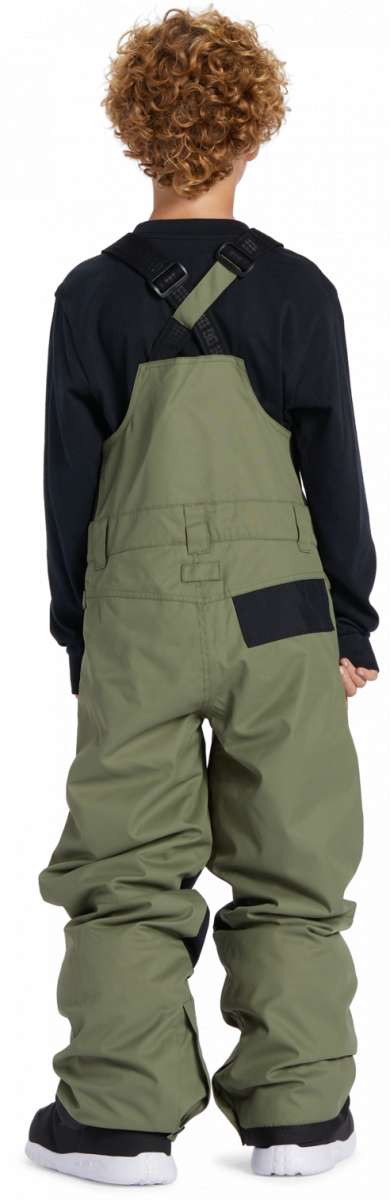 DC Youth Roadblock Insulated Bib - A young boy wearing olive green bib overalls with black straps and buckles, paired with a black long-sleeve shirt and white sneakers.