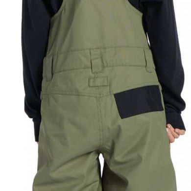 DC Youth Roadblock Insulated Bib - A young boy wearing olive green bib overalls with black straps and buckles, paired with a black long-sleeve shirt and white sneakers.