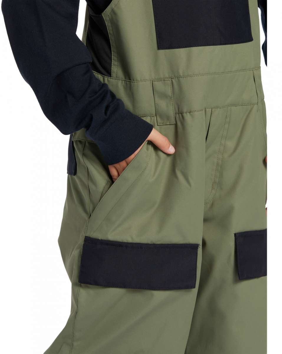 DC Youth Roadblock Insulated Bib 2024 - A pair of olive green insulated bib overalls with a black square patch on the right thigh and a black strap buckle on the left shoulder strap.