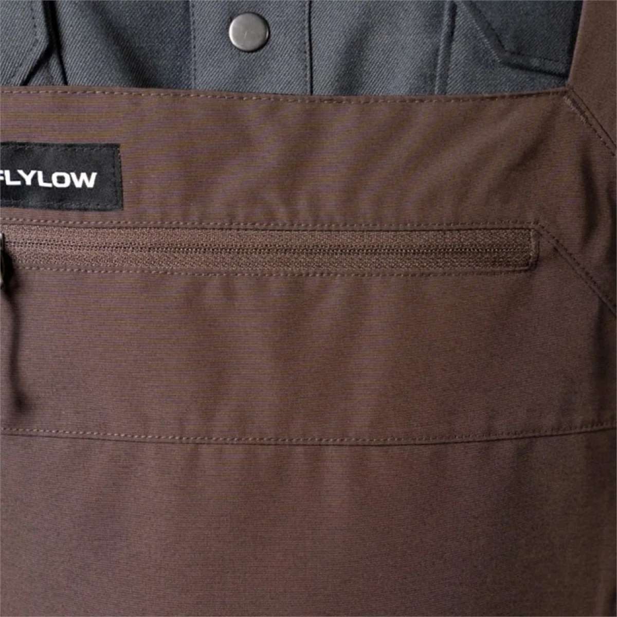 Flylow Firebird Shell Bib Pants 2024 - A pair of brown bib pants with a black patch on the left side featuring white lettering that reads "FLYLOW".