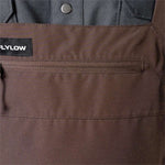 Flylow Firebird Shell Bib Pants 2024 - A pair of brown bib pants with a black patch on the left side featuring white lettering that reads "FLYLOW".