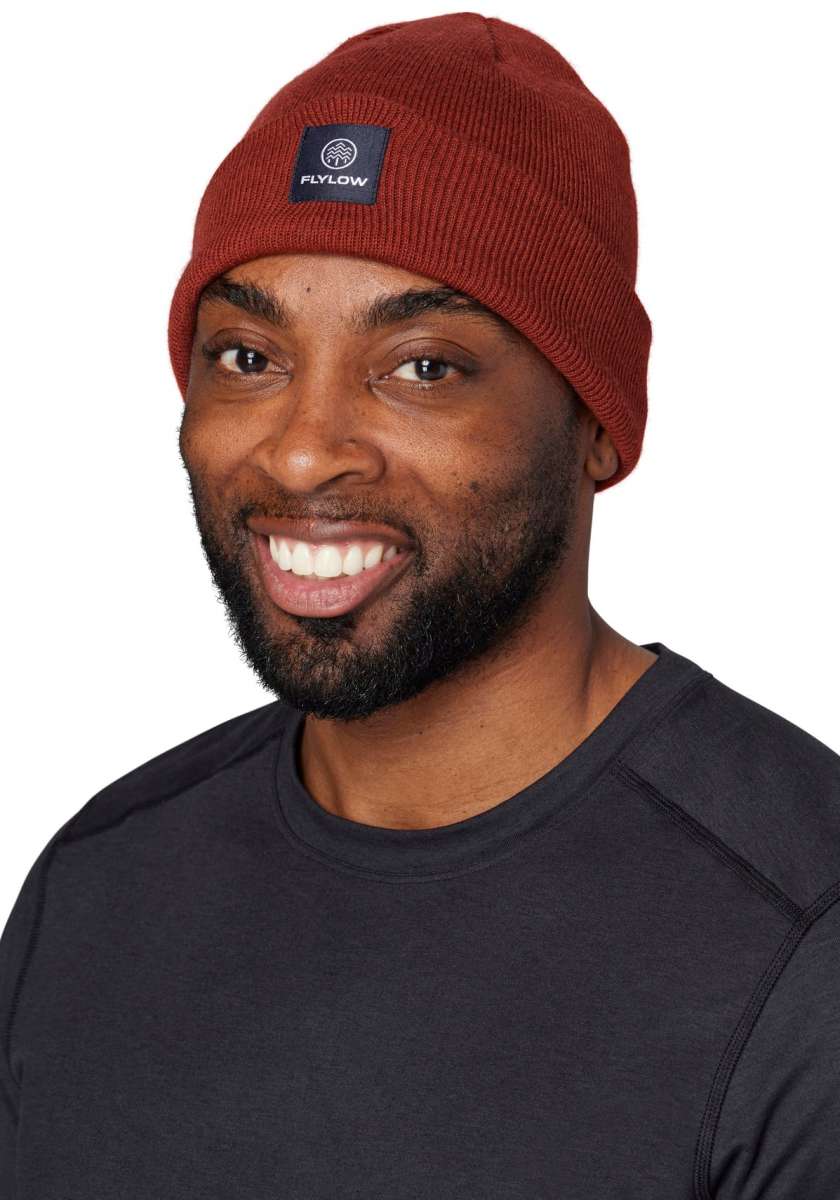Flylow Longshoreman Beanie 2024 - A rust-colored beanie with a black patch on the front featuring a white logo and the word "FLYLOW" in white letters.