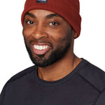 Flylow Longshoreman Beanie 2024 - A rust-colored beanie with a black patch on the front featuring a white logo and the word "FLYLOW" in white letters.