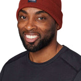 Flylow Longshoreman Beanie 2024 - A rust-colored beanie with a black patch on the front featuring a white logo and the word "FLYLOW" in white letters.