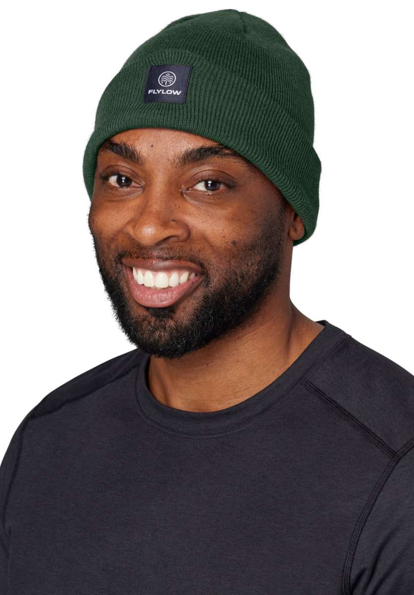 Flylow Longshoreman Beanie 2024 - A dark green beanie with a black patch on the front featuring a white logo and the word "FLYLOW" in white letters.