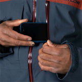 Flylow Quantum Pro Shell Jacket 2024 - A dark blue jacket with a burgundy zipper and trim, worn by a model in front of a snowy mountain backdrop.