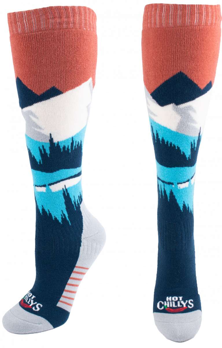 Hot Chillys Women's Mountains Mid Volume Sock 2024 - A pair of knee-high socks with a mountain design in shades of blue and white, featuring a red band at the top.