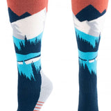 Hot Chillys Women's Mountains Mid Volume Sock 2024 - A pair of knee-high socks with a mountain design in shades of blue and white, featuring a red band at the top.