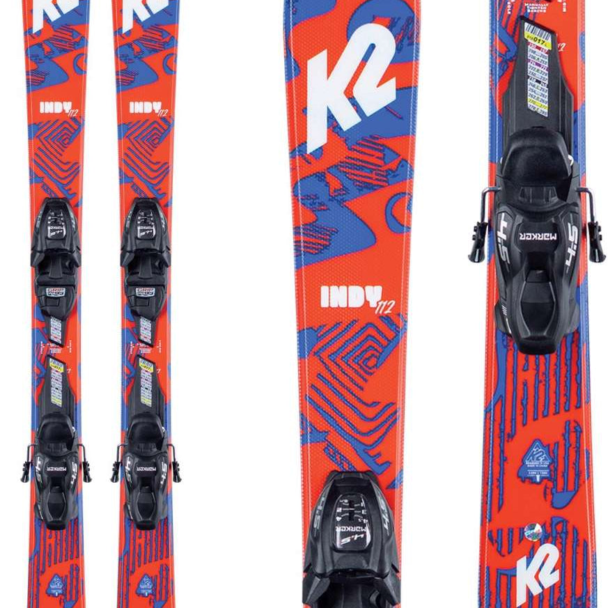 The image shows a pair of K2 Boys Indy Skis with FDT 4.5 Bindings for the 2021-2022 season. The skis are red and blue, featuring the K2 logo prominently on both sides. They have a unique design with abstract shapes and patterns that add to their visual appeal. The bindings are black and match the overall color scheme of the skis. The image is a product photo meant for an online store or catalog, providing potential buyers with a clear view of the item's details.