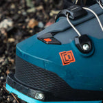 Blue K2 Mindbender 130 BOA ski boot with a white sole and red accent sits on a forest floor.