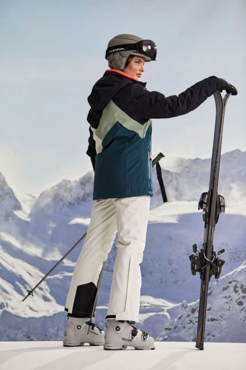 Killtec Ladies KSW 83 Peak Insulated Jacket - A dark blue jacket with a light green chevron pattern on the back, worn by a model in front of snowy mountains.