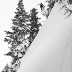 Lib Tech Skunk Ape Camber Snowboard 2025 - A snowboarder is seen from below, jumping off a steep snowy slope with trees in the background.