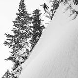 Lib Tech Skunk Ape Camber Snowboard 2025 - A snowboarder is seen from below, jumping off a steep snowy slope with trees in the background.