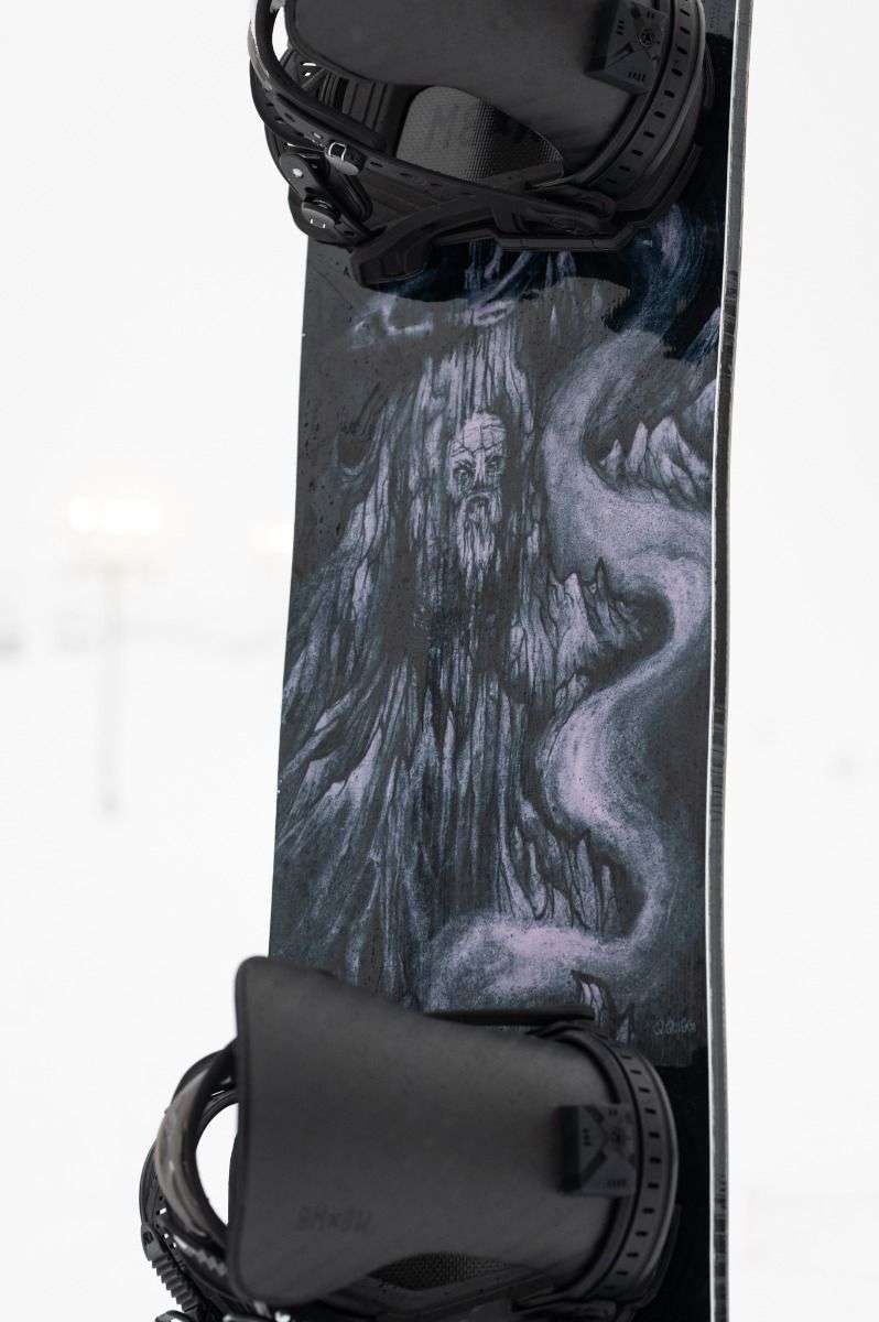 Lib Tech Skunk Ape Camber Snowboard 2025 - Black snowboard with a white and blue abstract design on top of a snowy mountain landscape.