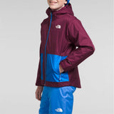 North Face Boys Freedom Triclimate Jacket 2024 - A boy wearing a maroon and blue jacket with a white logo on the left chest area.