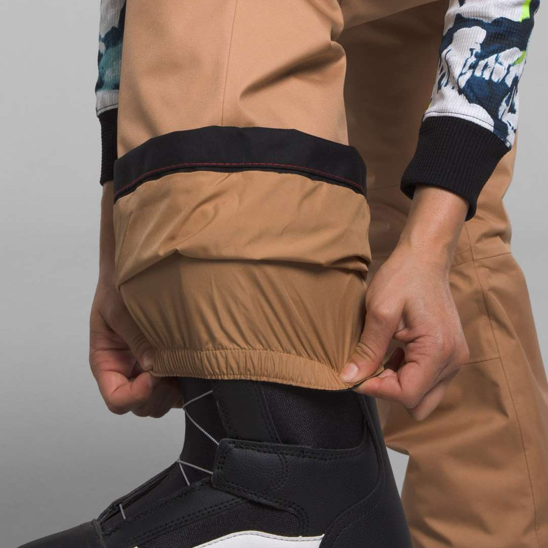 North Face Girls Freedom Insulated Pant 2024 - A pair of tan insulated pants with a black stripe at the top and a white logo on the left leg.