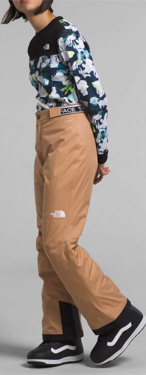 North Face Girls Freedom Insulated Pant 2024 - A young girl wearing a floral long-sleeve shirt and tan pants with a black waistband that reads "FACE THE" in white letters.