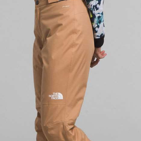 North Face Girls Freedom Insulated Pant 2024 - A young girl wearing a floral long-sleeve shirt and tan pants with a black waistband that reads "FACE THE" in white letters.