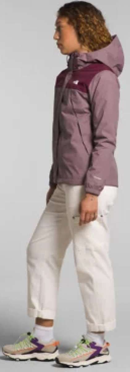 North Face Ladies Antora Triclimate Shell Jacket 2024 - A woman with curly brown hair wearing a purple jacket, white pants and green sneakers is shown from the side.