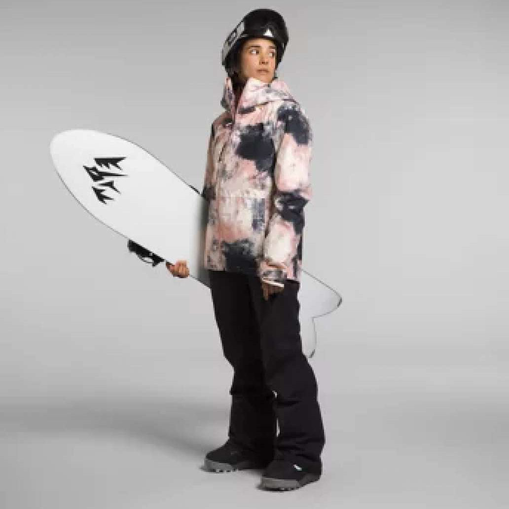 North Face Ladies Thermal Eco Snow Triclimate Jacket 2024 - A woman wearing a pink and black tie-dye patterned jacket with a hood, holding a snowboard in her left hand.