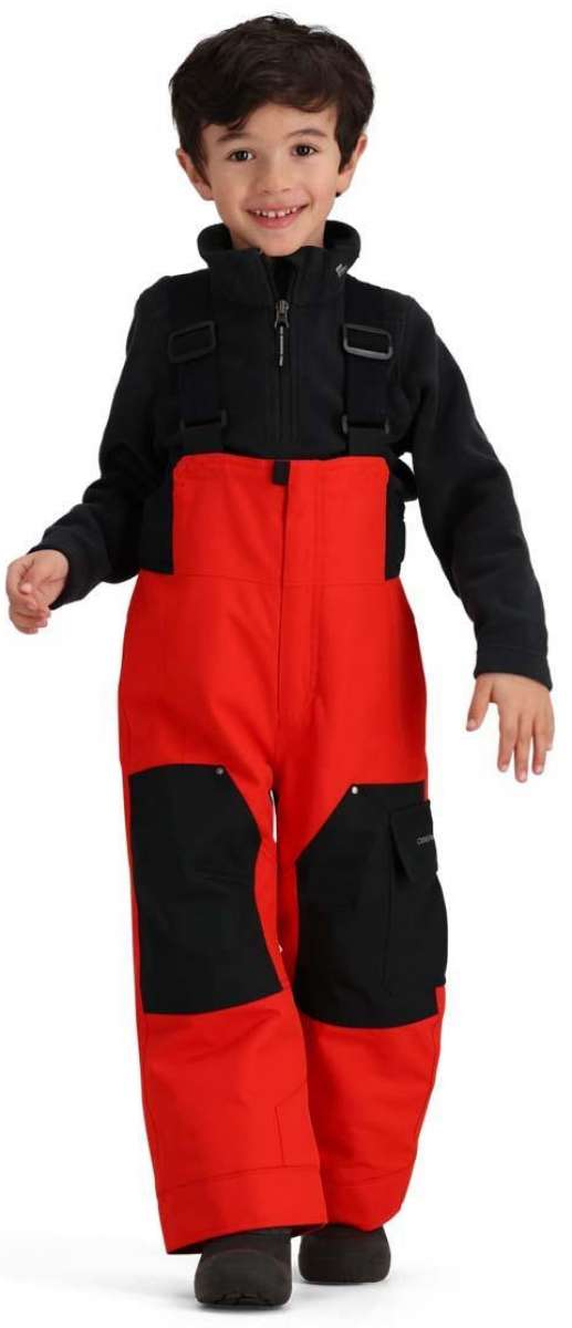 Obermeyer Juniors Volt Insulated Pant - Black snow pants with a subtle white pattern on the left leg, worn by a young girl in front of a blurred snowy background.