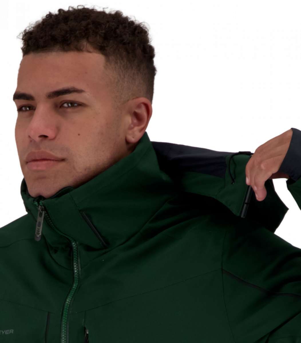 Obermeyer Kodiak Jacket 2022 - A dark green jacket with a high collar and zippered pockets, worn by a man with short curly hair looking to his left.