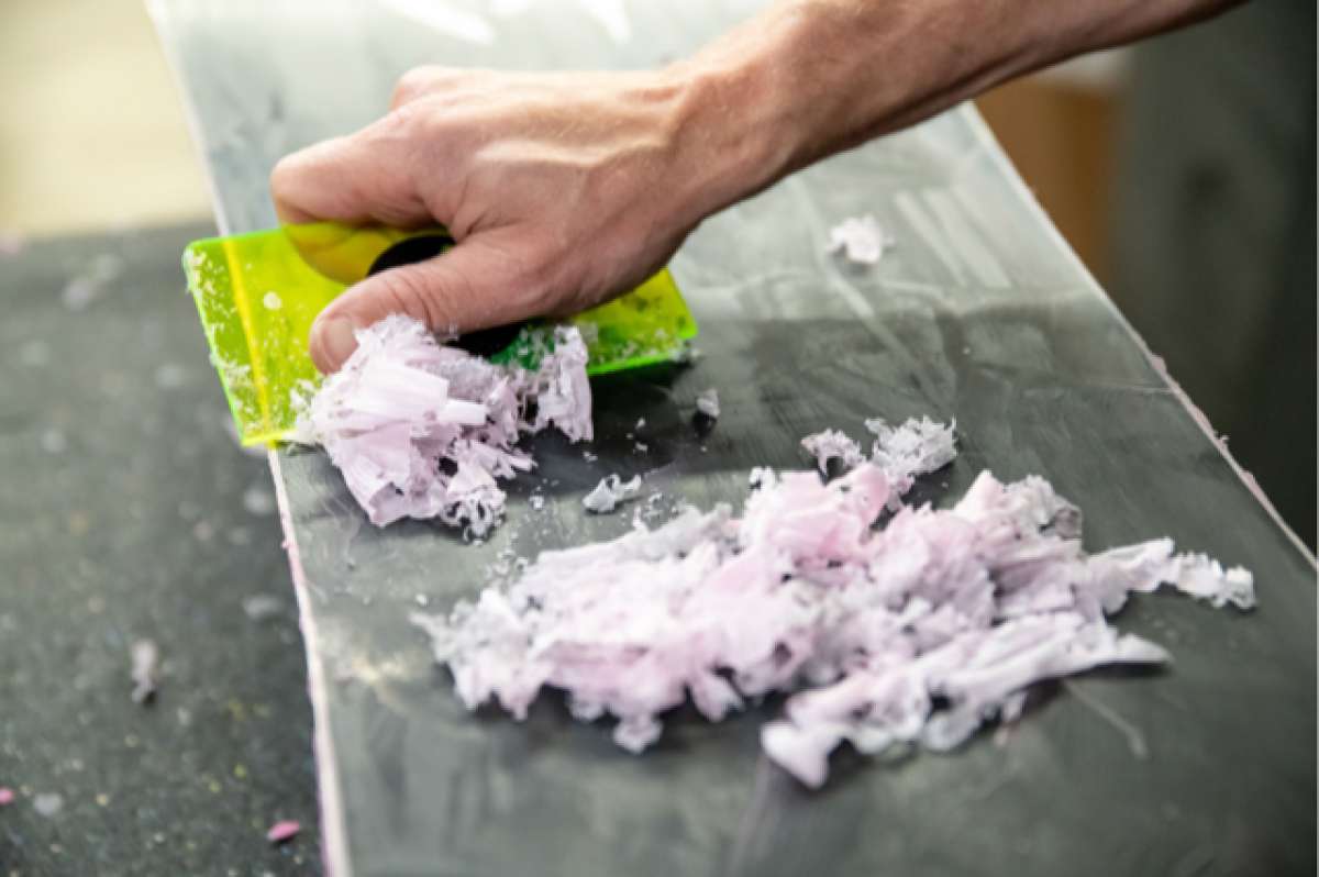 Oneball Shape Shifter Maple Bacon Wax 2024 - A green and yellow wax scraper with a black handle is shown on top of a pile of pinkish-white wax flakes.