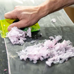 Oneball Shape Shifter Reeses Wax - A green rectangular wax scraper with a black handle, holding a small pile of white and pink wax shavings.