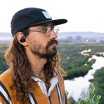 Outdoor Tech Mantas 2.0 Wireless Earbuds - Black earbuds with white accents and a charging case in the background.