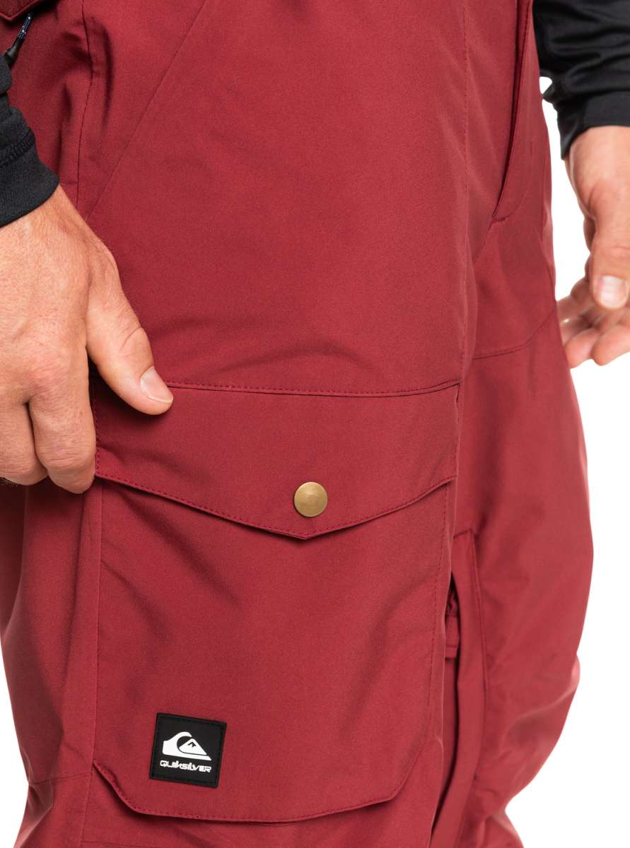 Quiksilver Utility Shell Pant 2023 - A pair of maroon snow pants with a black logo patch on the left leg featuring a white wave design and the word "Quiksilver" in white letters.