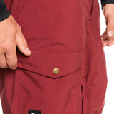 Quiksilver Utility Shell Pant 2023 - A pair of maroon snow pants with a black logo patch on the left leg featuring a white wave design and the word "Quiksilver" in white letters.